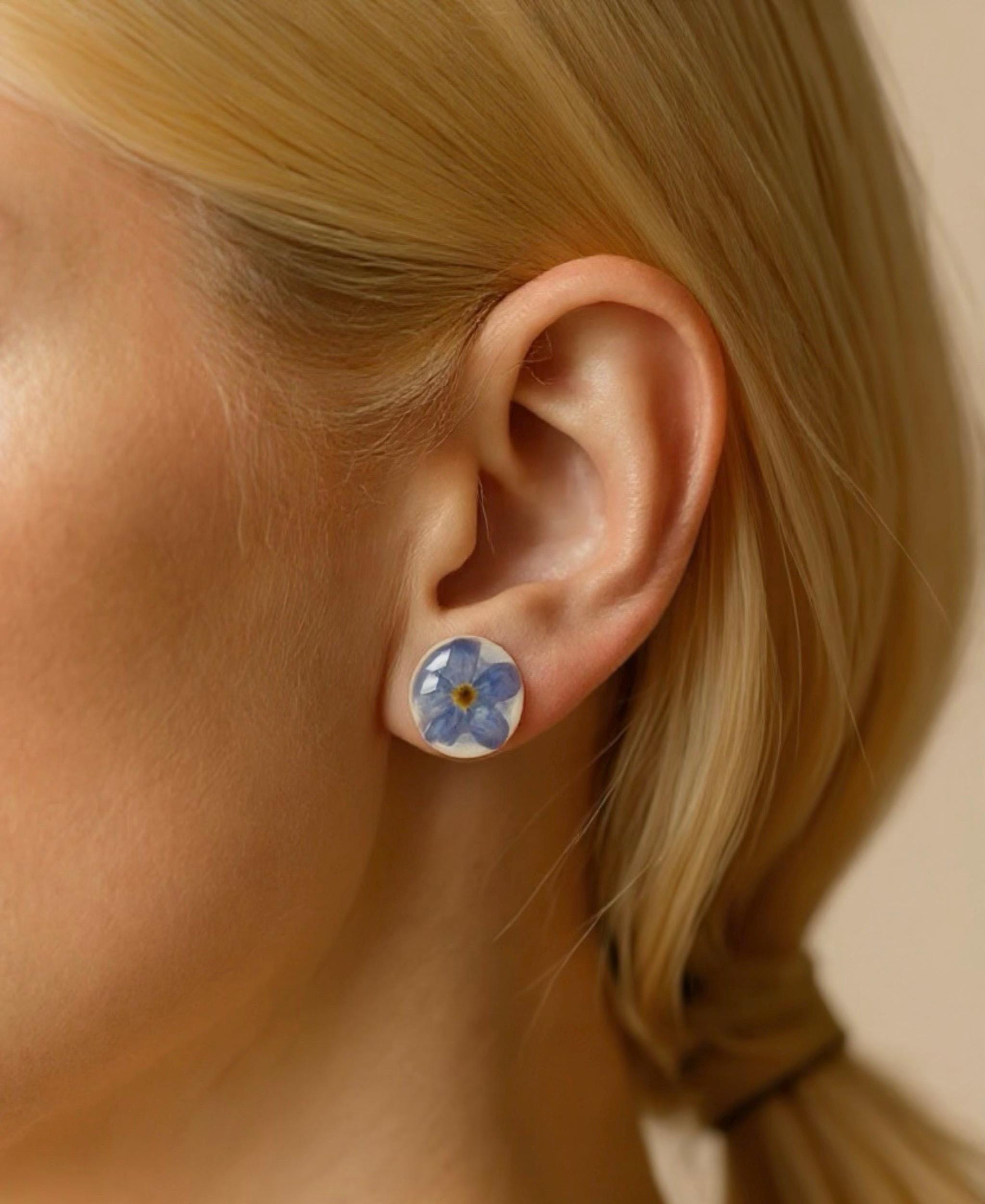 Close up of a woman wearing forget me not stud earrings