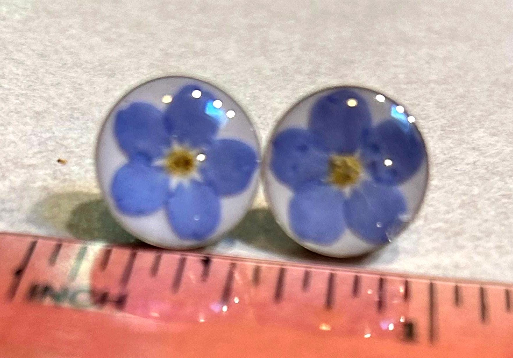 Pair of earrings with blue flower design on a white background with a ruler for scale.