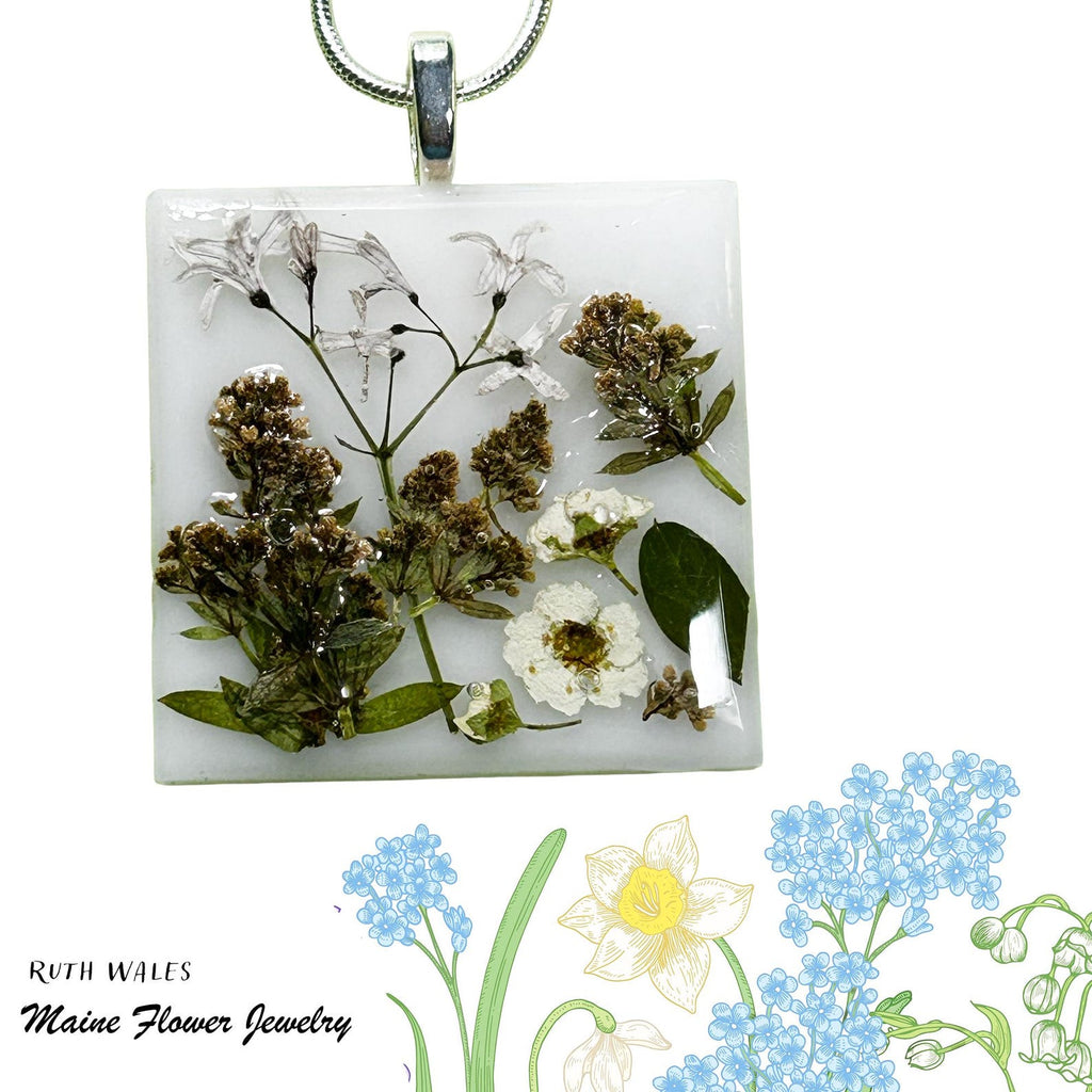 Square pendant with pressed flowers and greenery on a white background, featuring 'Ruth Wales Maine Flower Jewelry'.